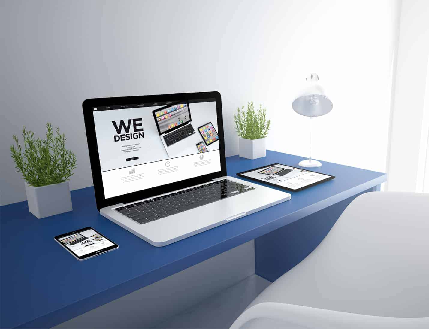 Web design from EWD (Esthetig Web Design) web design page - WordPress. Image shows a tablet, laptop and phone all with the same website on, either side is a plant in a white square pot, to the right is a white lamp, they all sit on a blue desk with a white chair in front, the wall behind is pale grey.